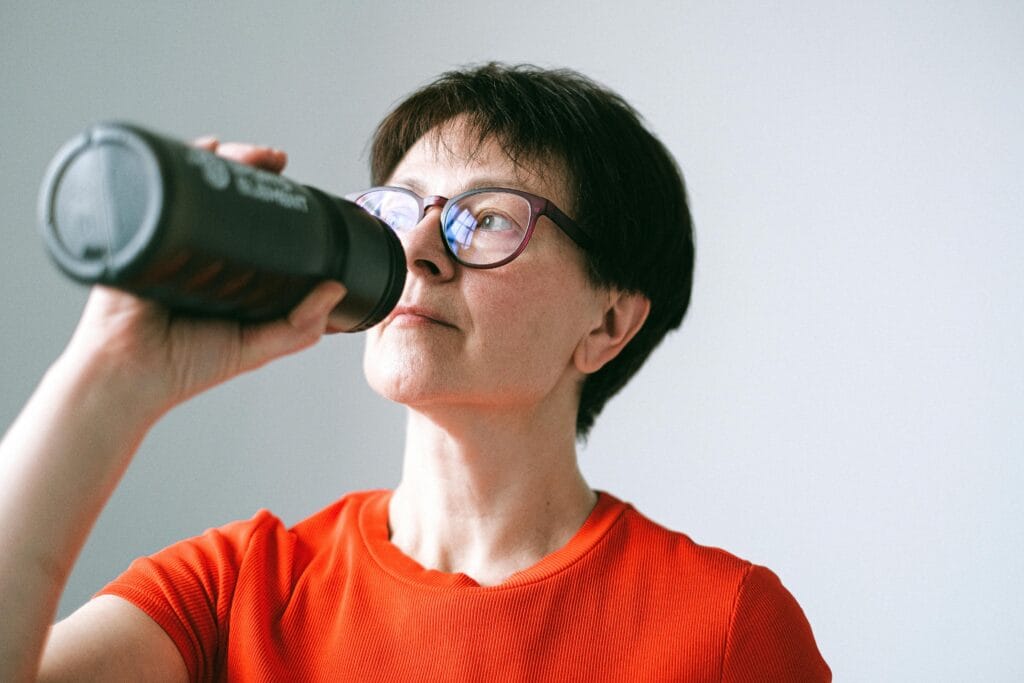 Caucasian senior woman in glasses drinking from a bottle, promoting active lifestyle.