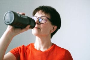 Caucasian senior woman in glasses drinking from a bottle, promoting active lifestyle.