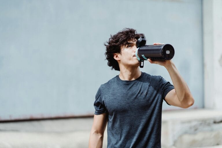 Man in a casual outfit drinking water from a bottle outdoors, focused on fitness and hydration.