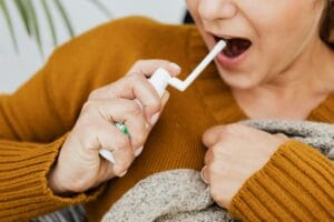 Close-up of a woman using oral spray for throat relief indoors.