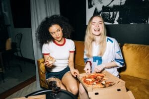 Two young women enjoying a fun pizza night at home, sharing laughter and joy.