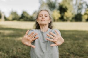 Elderly woman meditating and stretching in a peaceful outdoor setting.