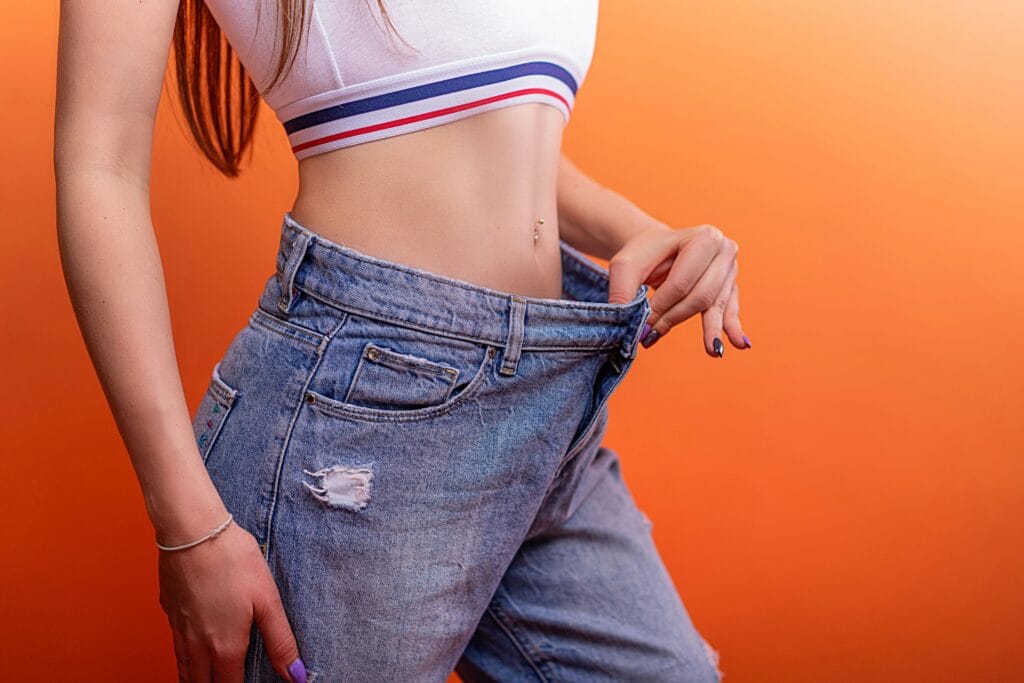 A woman holding loose jeans against her slim waist, symbolizing successful weight loss.