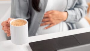woman with a stomach ache holding a cup of coffee | gut health