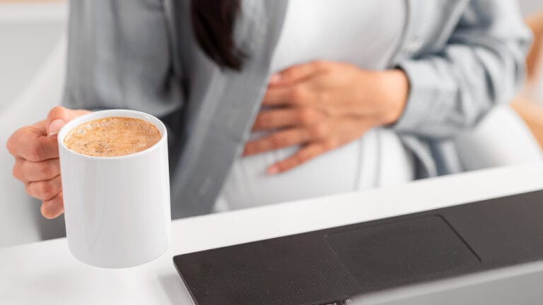 woman with a stomach ache holding a cup of coffee | gut health