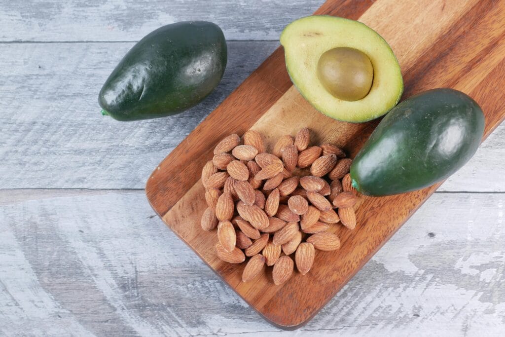 Top view of fresh avocados and almonds on a wooden board for a healthy snack.