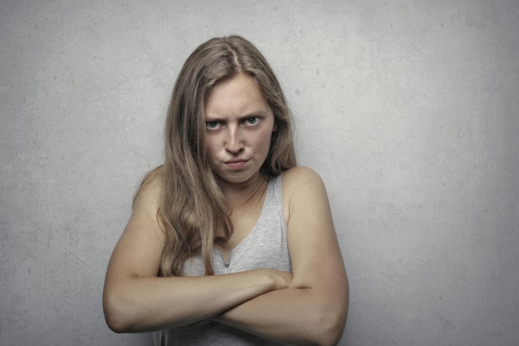 A woman with arms crossed showing a fierce expression against a gray background.