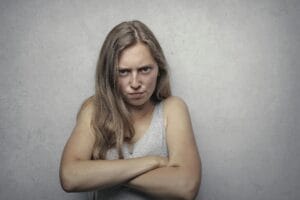A woman with arms crossed showing a fierce expression against a gray background.