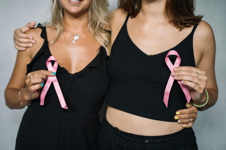 Two women showing support for breast cancer awareness by holding pink ribbons.