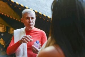 Elderly man in a red shirt with towel and water bottle during a gym break in Portugal.