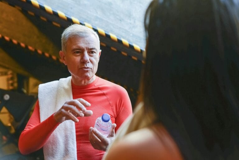 Elderly man in a red shirt with towel and water bottle during a gym break in Portugal.