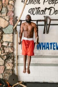 Fit man performs strength workout on gymnastic rings in gym setting, showcasing athleticism.