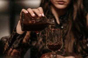 A woman in leopard print pours a dark liquid into a crystal glass, suggesting mystery.