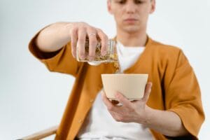 A man in a brown shirt pours cereal from a glass jar into a bowl, focused on the task.