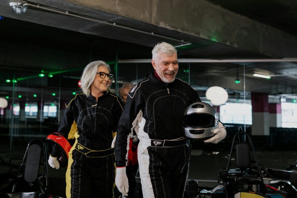 A happy senior couple wearing racing suits and helmets, ready for indoor kart racing.