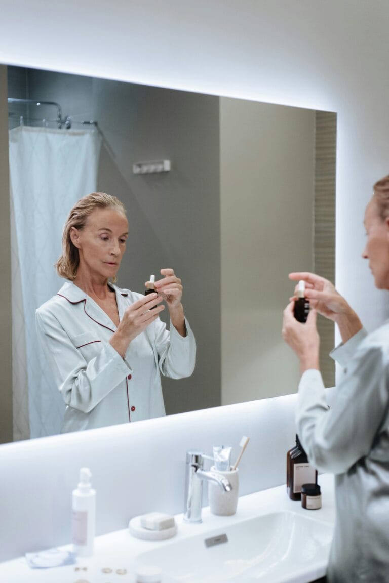 Elderly woman in pajamas using skincare serum while looking at her reflection in a modern bathroom. skin
