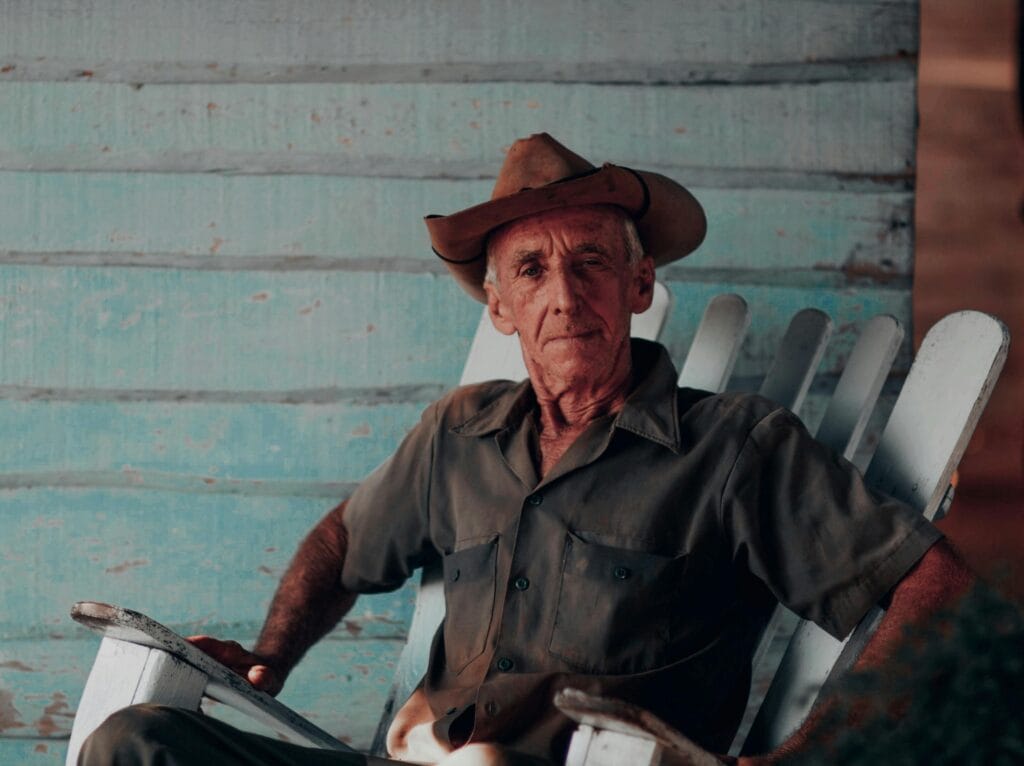 Senior man enjoying leisure time outdoors in a rustic setting on a wooden rocking chair.