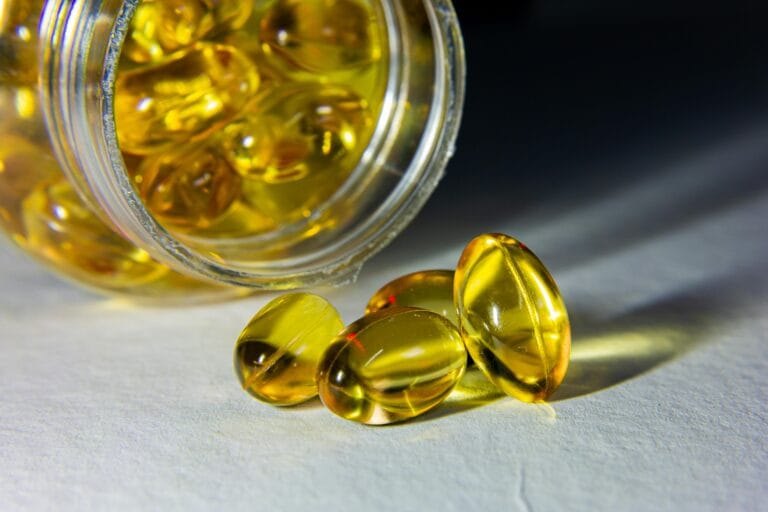 Close-up of golden softgel capsules spilled from an open bottle on a white surface. | vitamins