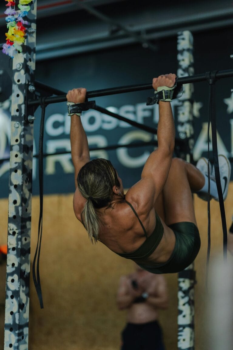 Athletic woman demonstrates strength with a pull-up in a gym environment, showing dedication and focus. | fit woman doing a pull up variation