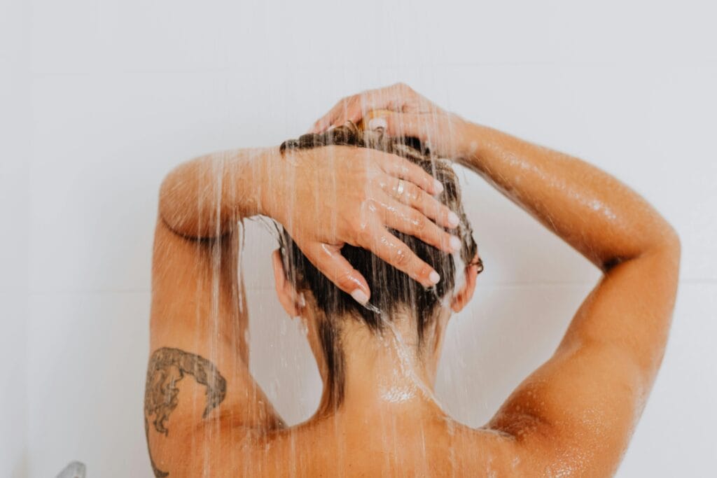 Person taking a shower, showcasing a tattoo on the arm and water flowing down.