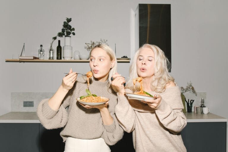 A candid moment of a mother and daughter enjoying homemade pasta together in a cozy kitchen.
