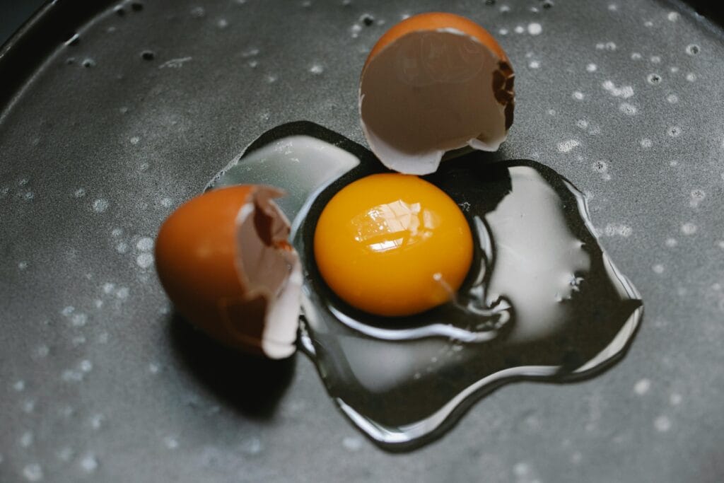 A raw egg with broken shells on a dark cooking surface, ideal for culinary and food photography.