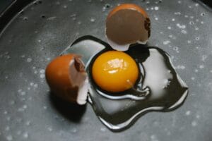 A raw egg with broken shells on a dark cooking surface, ideal for culinary and food photography.
