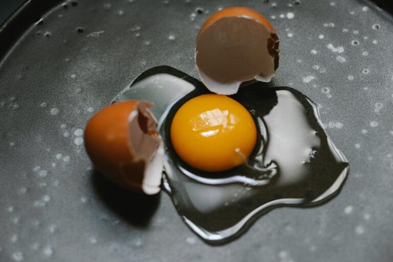 A raw egg with broken shells on a dark cooking surface, ideal for culinary and food photography.