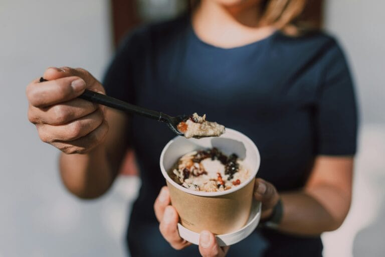 Close-up of a person holding a bowl of vegan oatmeal topped with fruits.