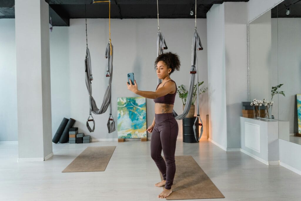 Woman in activewear taking a selfie in a modern aerial yoga studio with hammocks.