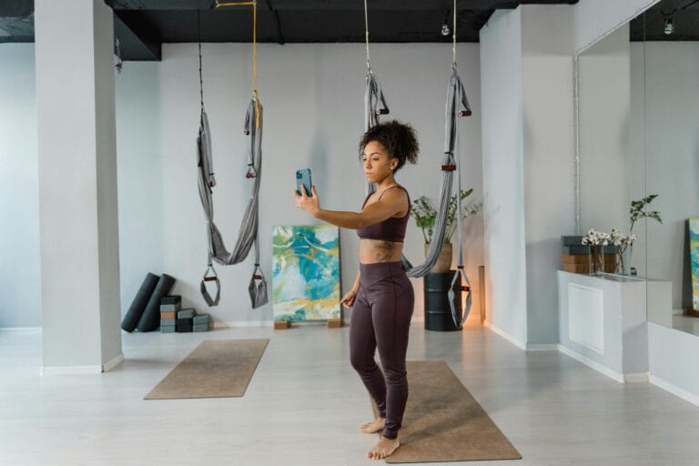 Woman in activewear taking a selfie in a modern aerial yoga studio with hammocks.