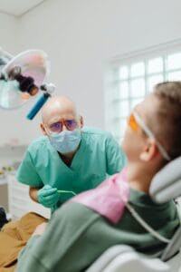 A dentist in a clinic providing dental care to a patient wearing safety glasses. | teeth