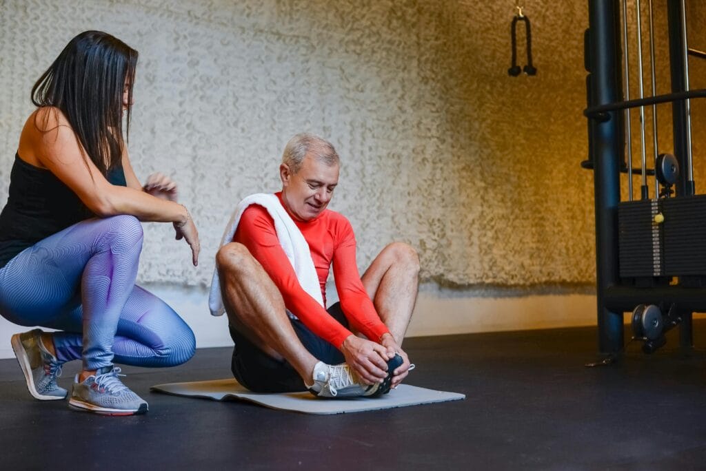 Senior man stretching on yoga mat with coach in gym for a healthy lifestyle.
