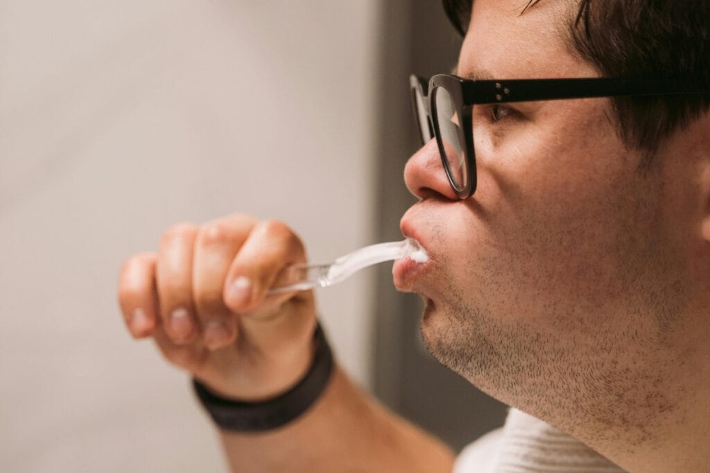 Side view of a man with glasses practicing oral hygiene by brushing teeth indoors.