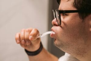 Side view of a man with glasses practicing oral hygiene by brushing teeth indoors.
