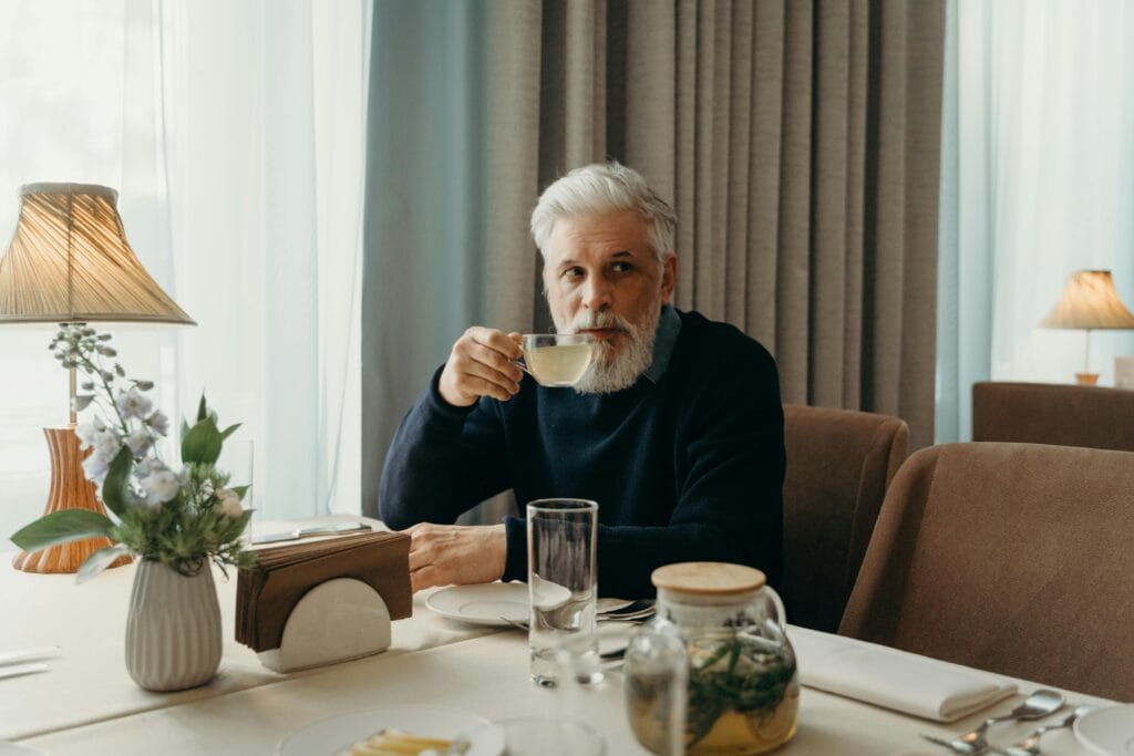 Elderly man with grey hair sipping tea in a peaceful and warm indoor setting.