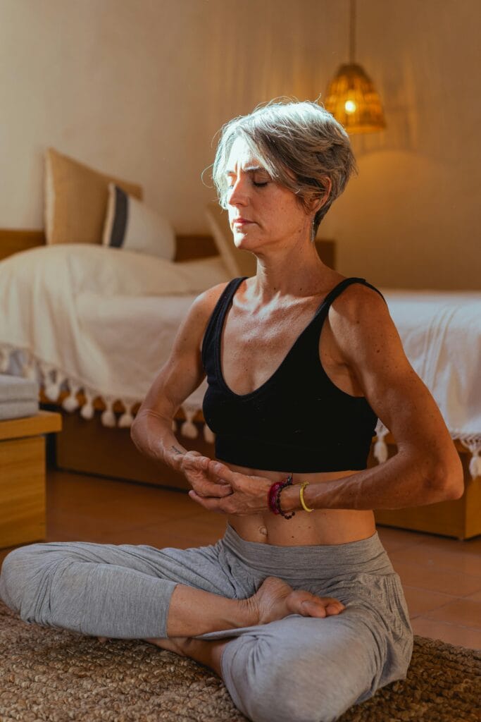 A senior woman meditates in a serene indoor setting, focusing on wellness and tranquility.