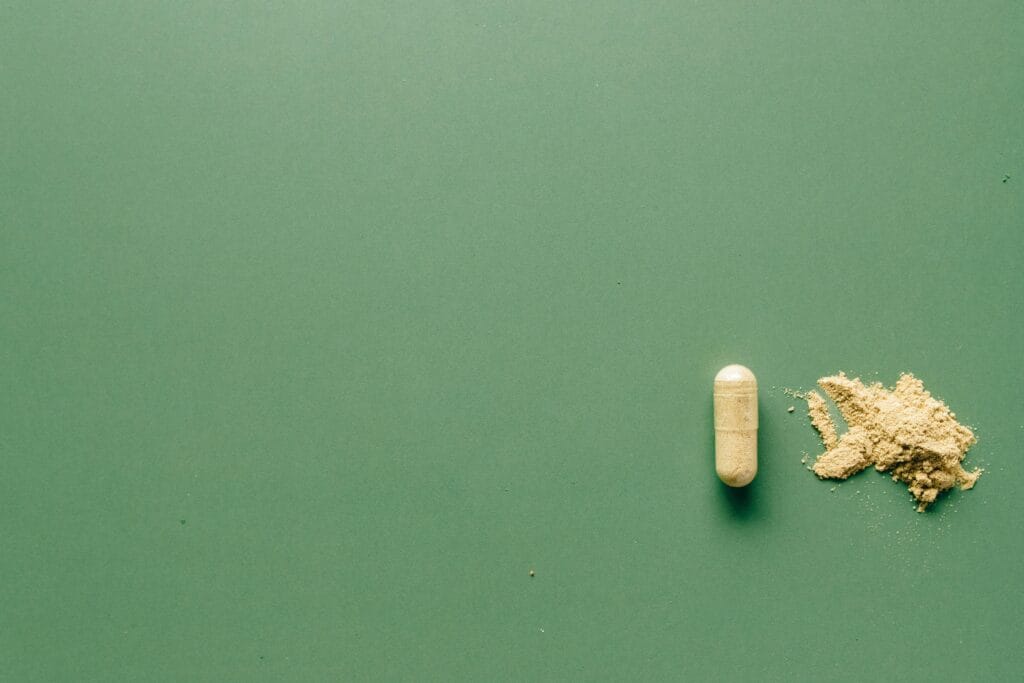 Close-up of herbal supplement capsule and powder on a minimalist green surface.
