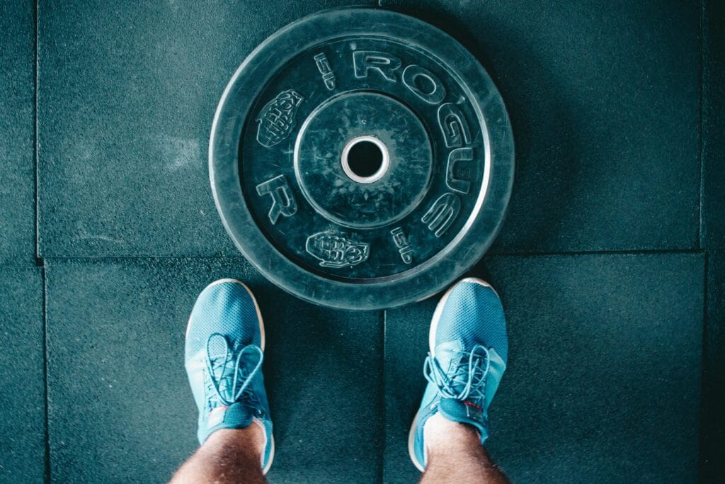 Blue sneakers next to a weight plate on a gym floor, top view.