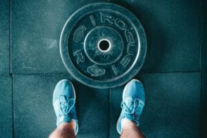 Blue sneakers next to a weight plate on a gym floor, top view.