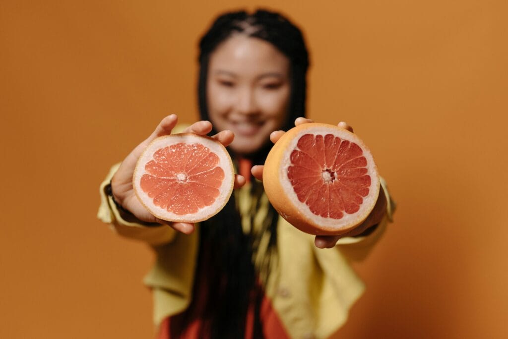 Bright studio shot featuring a woman holding sliced grapefruit with an orange background.