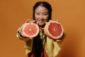 Bright studio shot featuring a woman holding sliced grapefruit with an orange background.