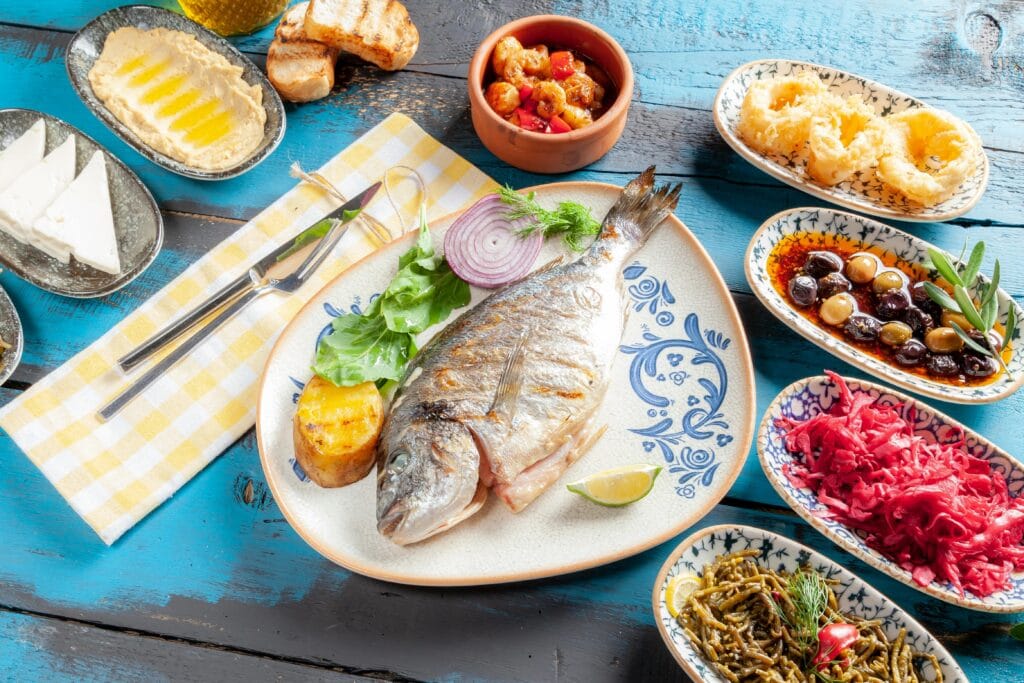 A vibrant Mediterranean meal featuring grilled fish and assorted appetizers on a rustic table.