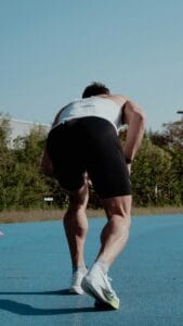 A male athlete gets ready at the starting line on a bright, sunny outdoor track.