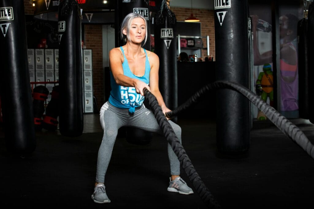 Woman working out with battle ropes in a gym, promoting a healthy lifestyle.