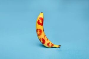 A banana adorned with red lipstick kiss marks against a vibrant blue background.