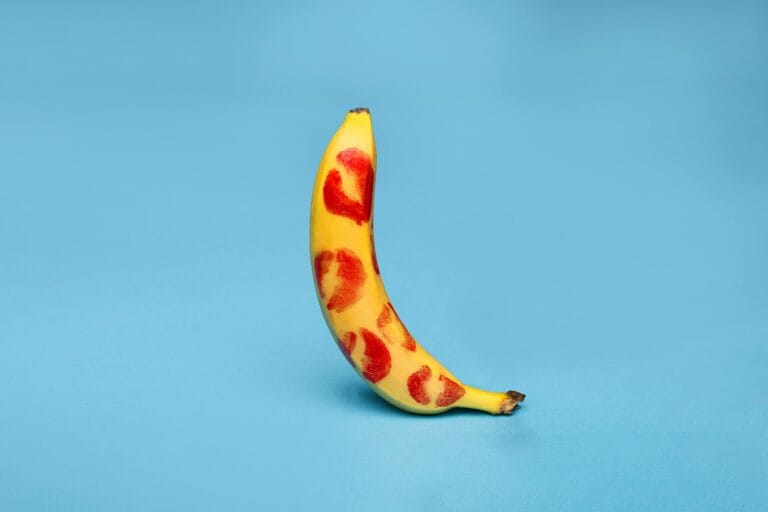 A banana adorned with red lipstick kiss marks against a vibrant blue background.