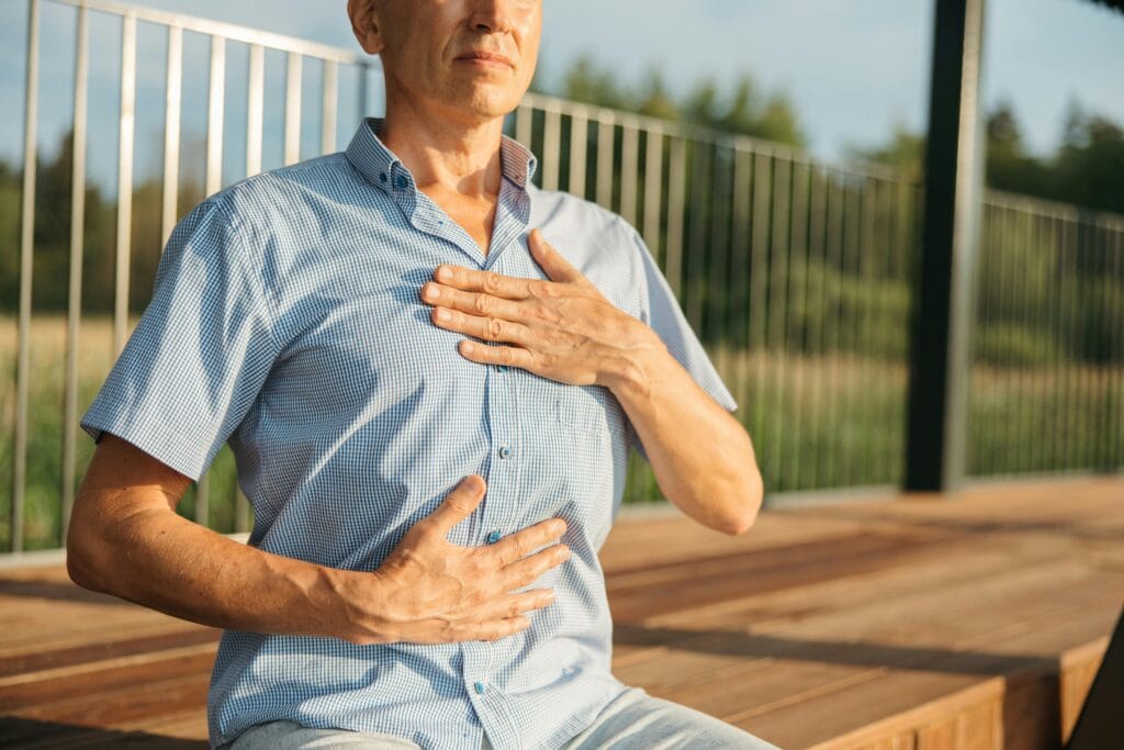 A man practicing relaxation with hands on chest and abdomen outdoors.