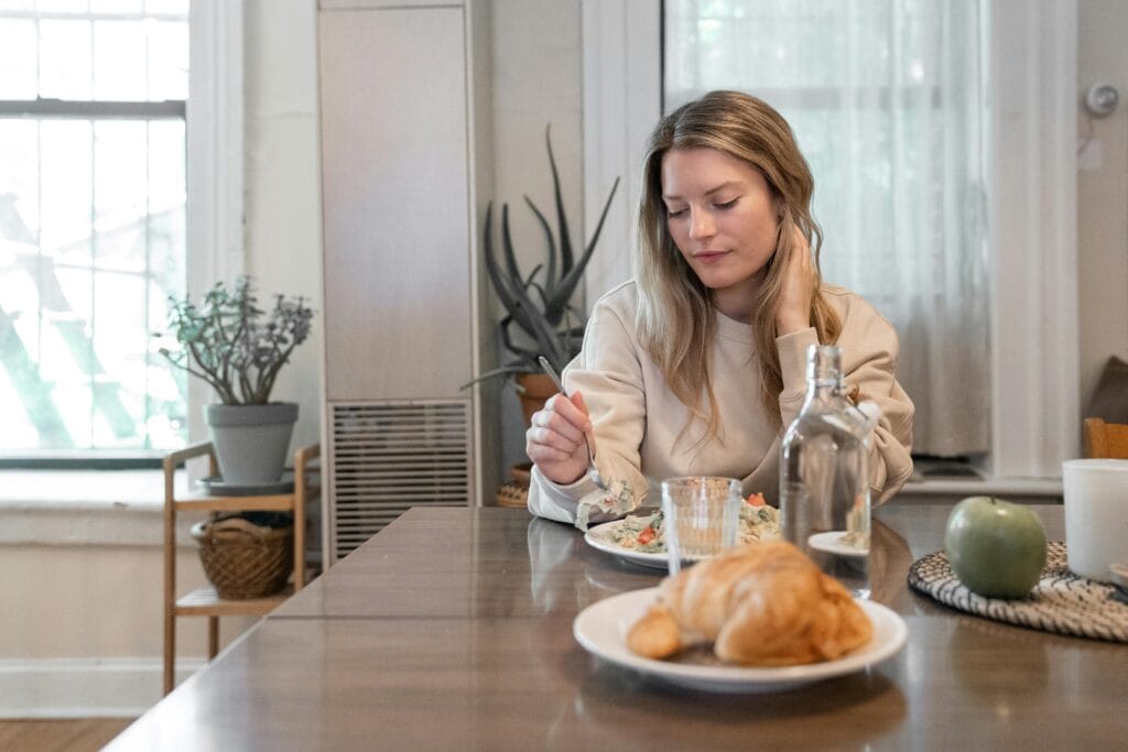 A woman indulging in a healthy salad at a cozy indoor setting, promoting wellness.