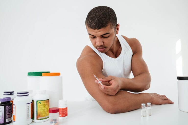 Sportsman standing over white wall holding syringle make injection | steriod, peptide